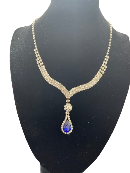Silver rhinestone necklace with blue teardrop pendant displayed on black stand
