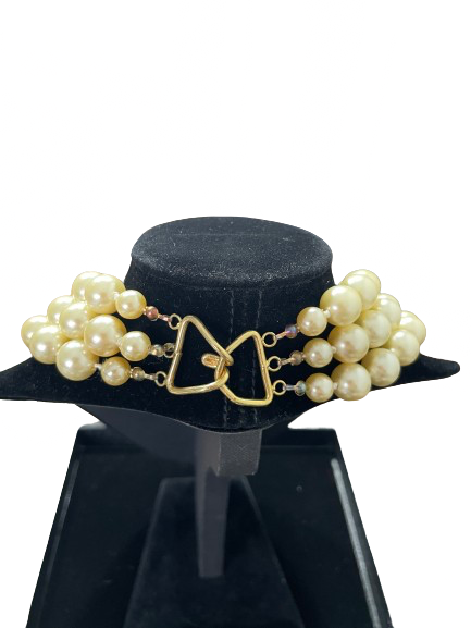 Pearl necklace with gold clasp on a black stand against a white background