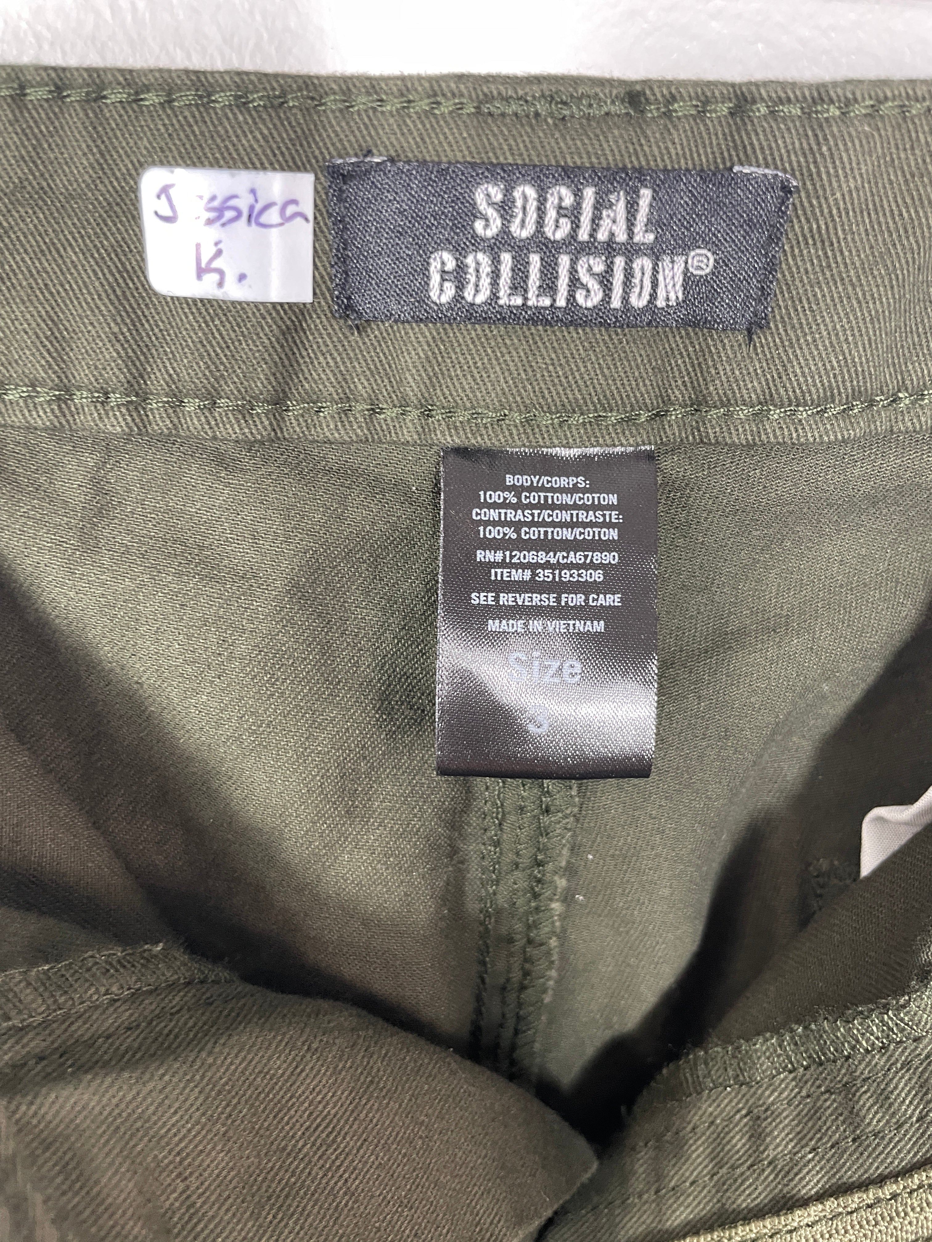 Close-up of inner waistband showing "Social Collision" label and handwritten "Jessica R." wardrobe tag.
