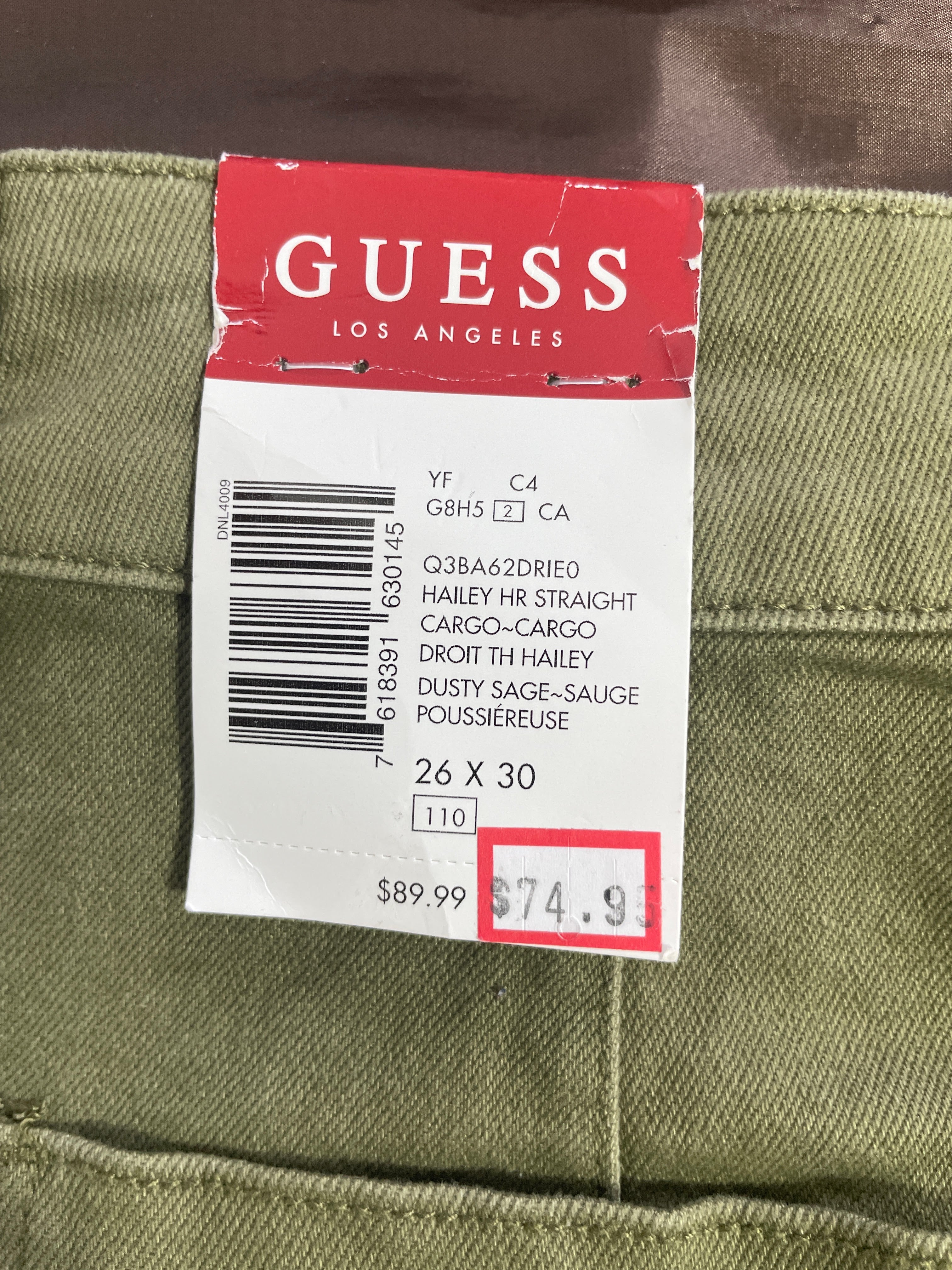 Close-up of the original Guess retail tag indicating the "Dusty Sage" color, size 26x30, and original $89.99 MSRP.