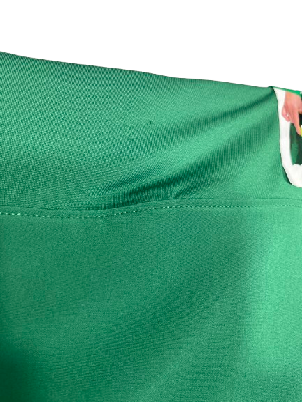 Close-up of a bright green athletic fabric garment, showing the texture of the material and a white trim detail on the right side.