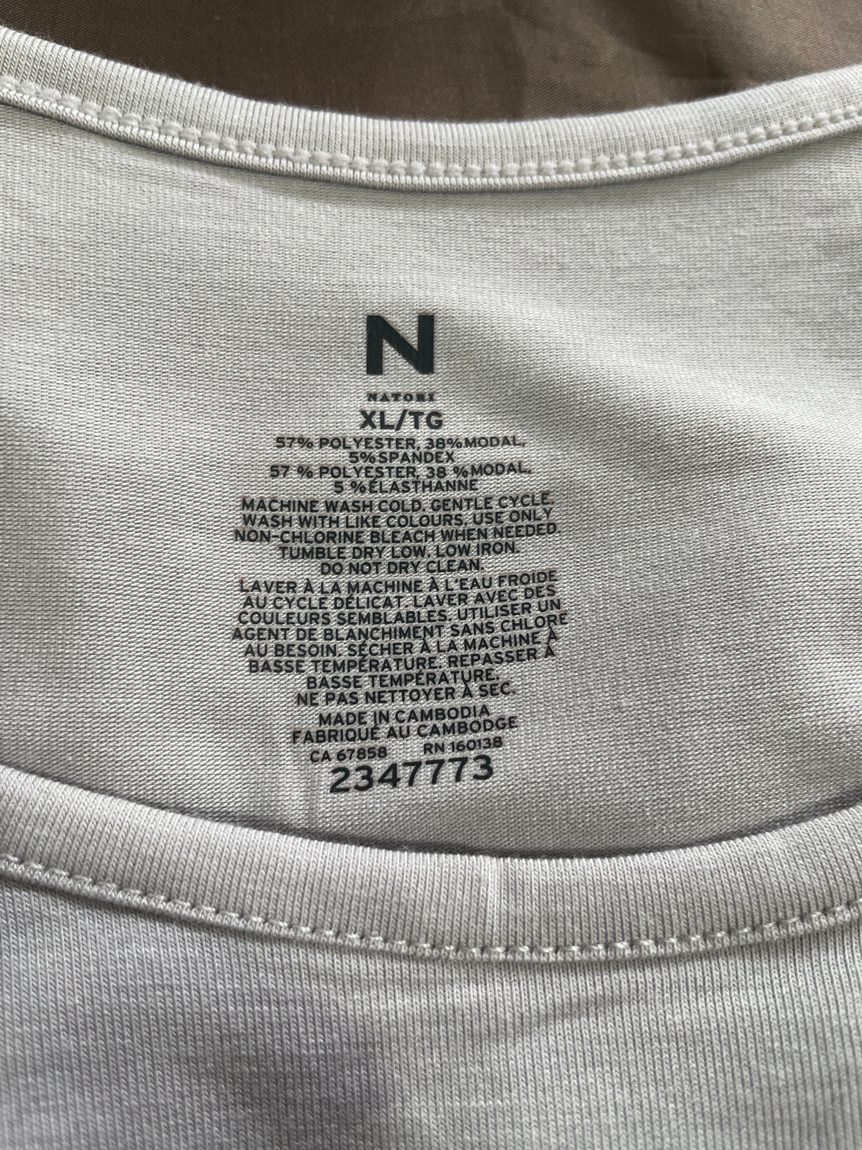 Close-up of the inside neck label of a light gray or off-white t-shirt, showing the brand 'N' and care instructions printed in black.