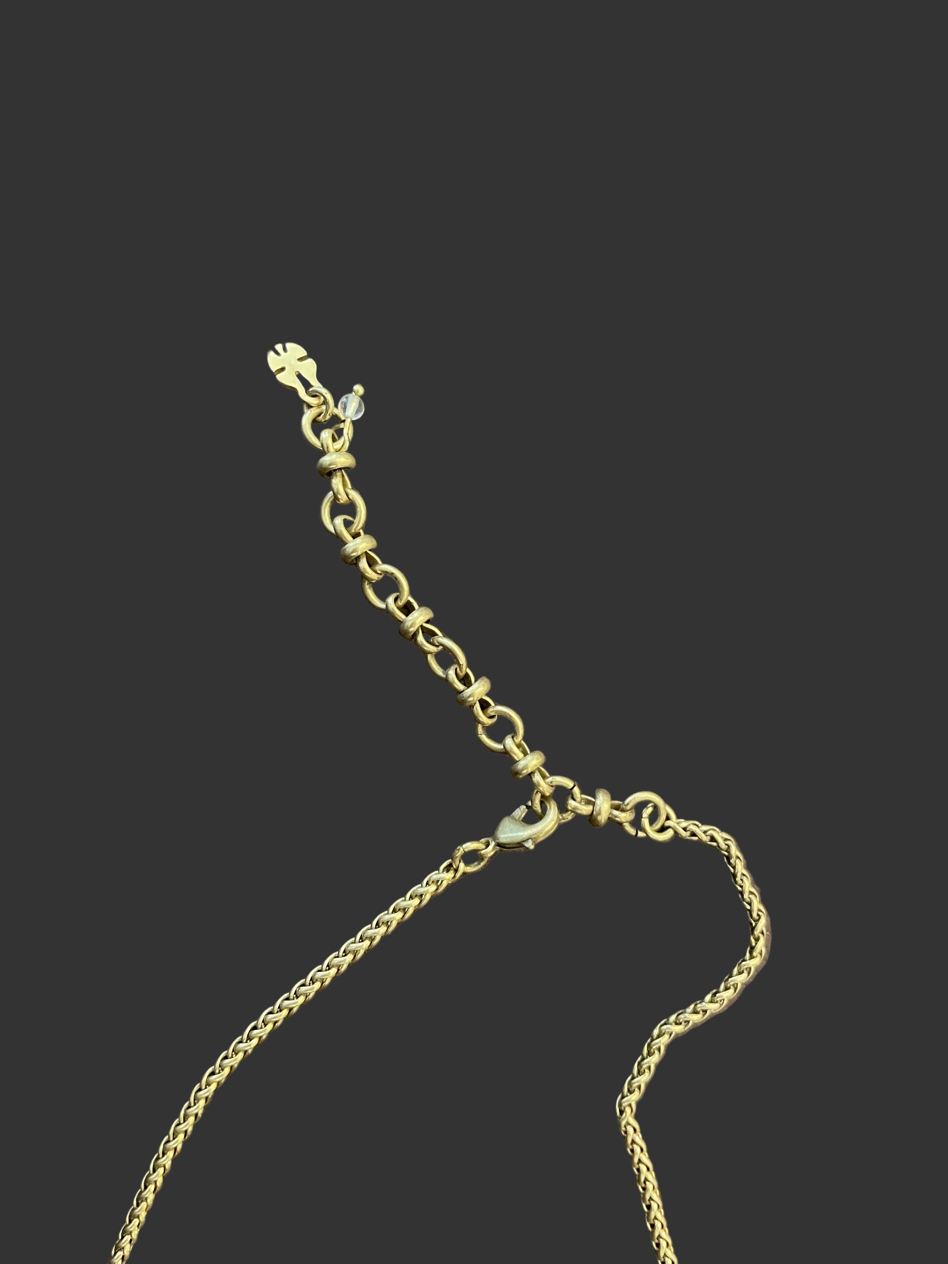 A close-up of a gold-toned chain extender with a lobster clasp and small charm, laid on a brown textured leather surface.
