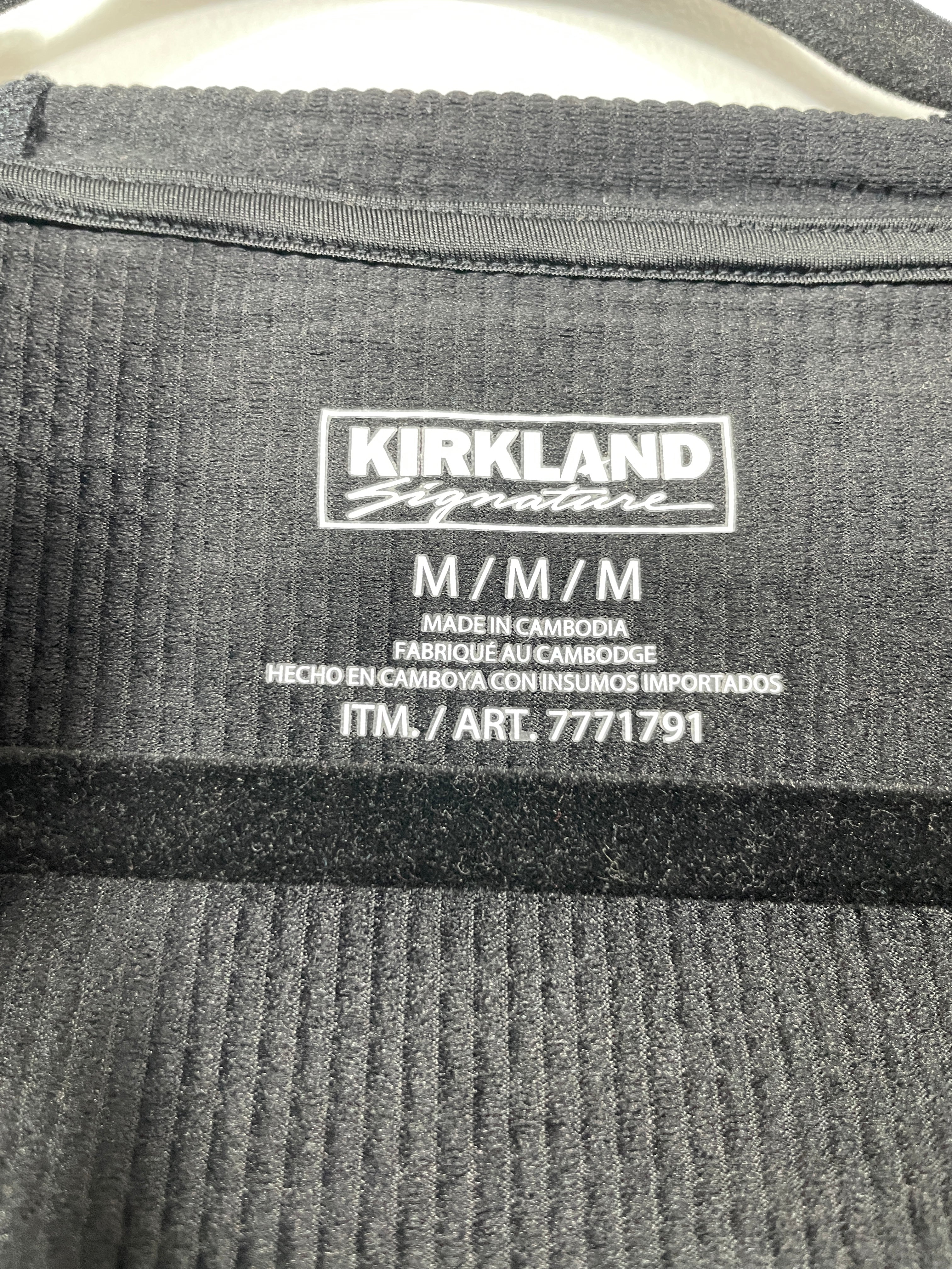 Close-up of a dark gray ribbed knit garment label reading Kirkland Signature, with size text M/M/M and product details below.