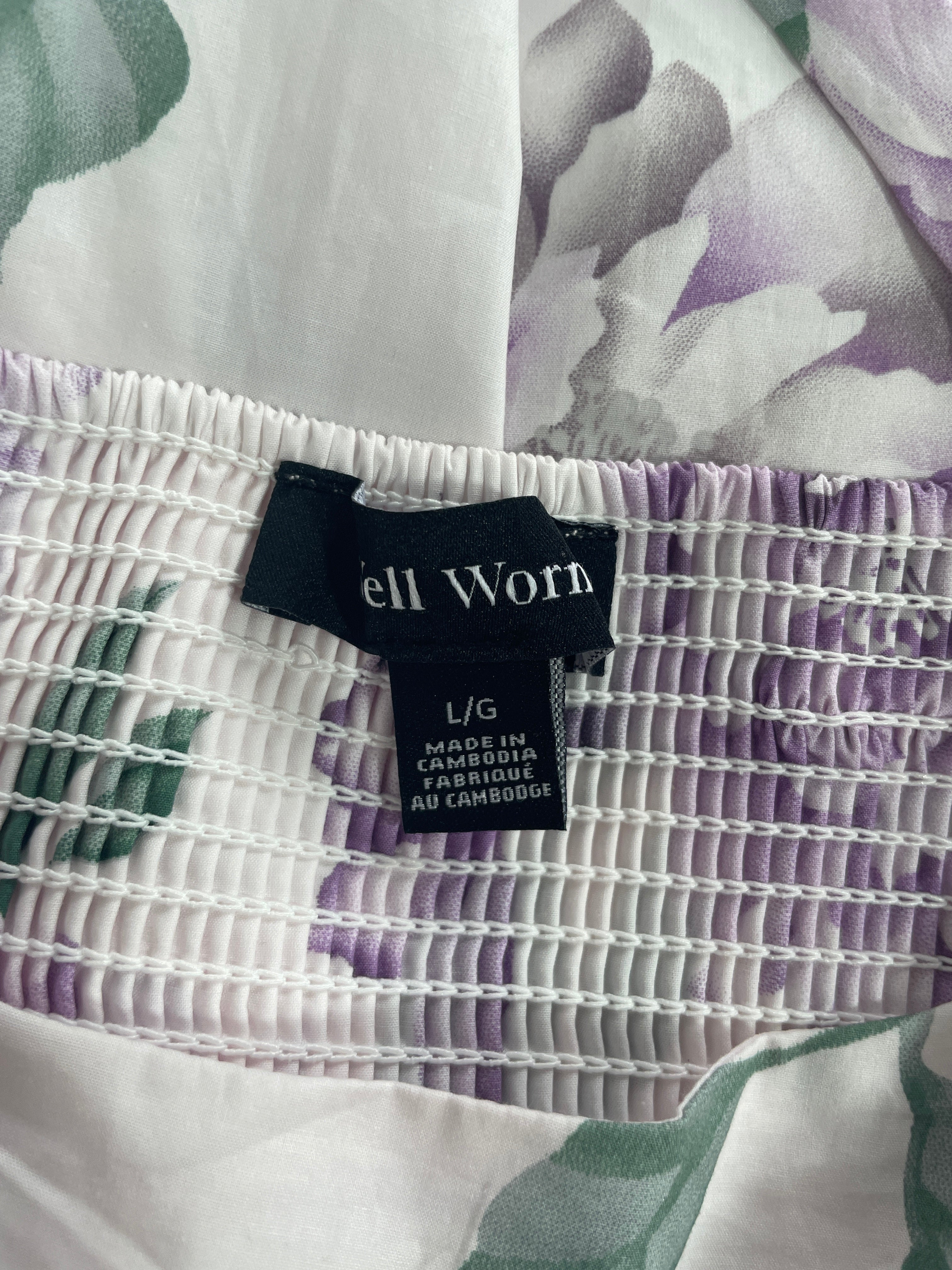 Close-up of a garment's smocked elastic waistband with a black 'ell Worn' brand label, showing a white and purple floral patterned fabric.