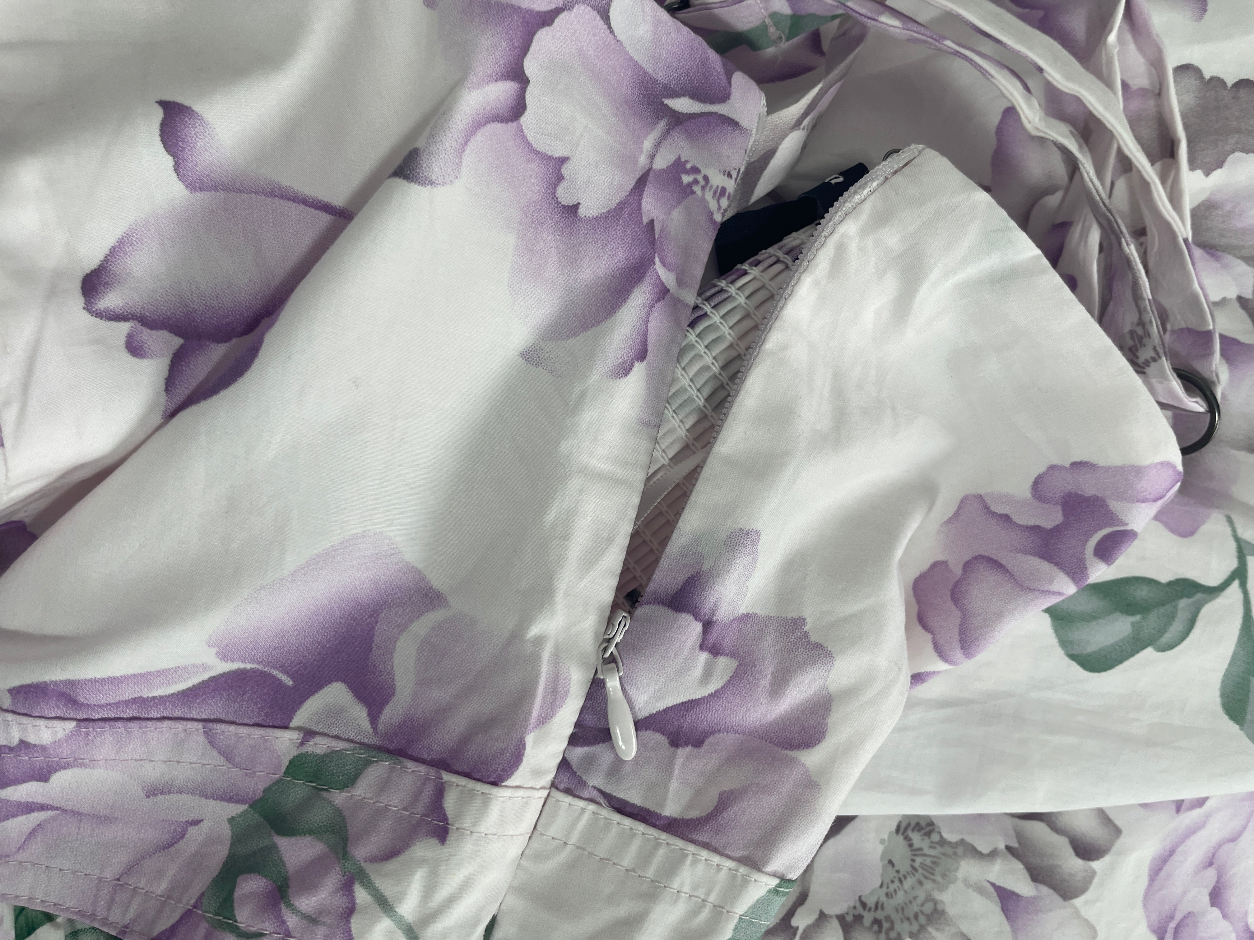 A close-up of a white fabric garment with a purple watercolor floral print, showing a zipper and drawstring detail.